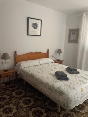 Un lit simple avec une couvre-lit à motifs floraux, deux lampes de chevet, un tableau encadré au mur et un sol à motifs.