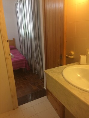 Une salle de bain avec un lavabo et des toilettes, une porte en bois et un lit avec un rideau à rayures.