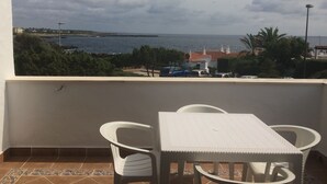 Een balkon met een tafel en stoelen, met uitzicht op de kust, gebouwen en een pier.