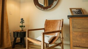 Une chaise en bois avec un coussin, un miroir rond accroché au mur, une petite table avec une plante et un meuble en bois.