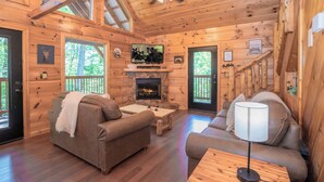 Interior acogedor de una cabaña con paredes de madera, chimenea, televisor y dos sofás.