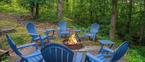 A circular seating arrangement around a central fire pit in a forested area.
