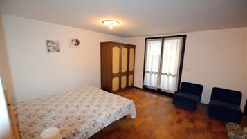 A bedroom with a bed, a wardrobe, two chairs, a window with curtains, and a ceiling light.