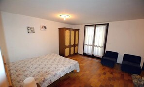 Une chambre à coucher comprenant un lit, une armoire, deux chaises, une fenêtre avec des rideaux et un luminaire au plafond.