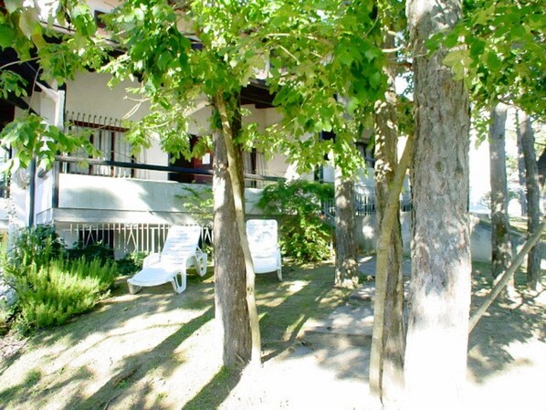 Une cour intérieure avec des arbres, un bâtiment blanc et deux fauteuils de jardin blancs.