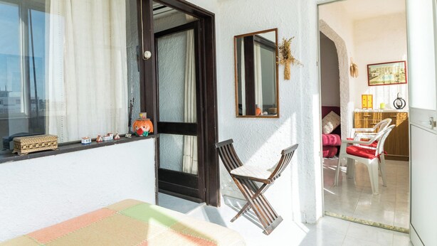 A room with a window, a mirror, a small table, and a chair.