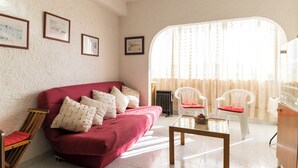 A living room with a red sofa, white chairs, a wooden coffee table, and framed pictures on the wall.