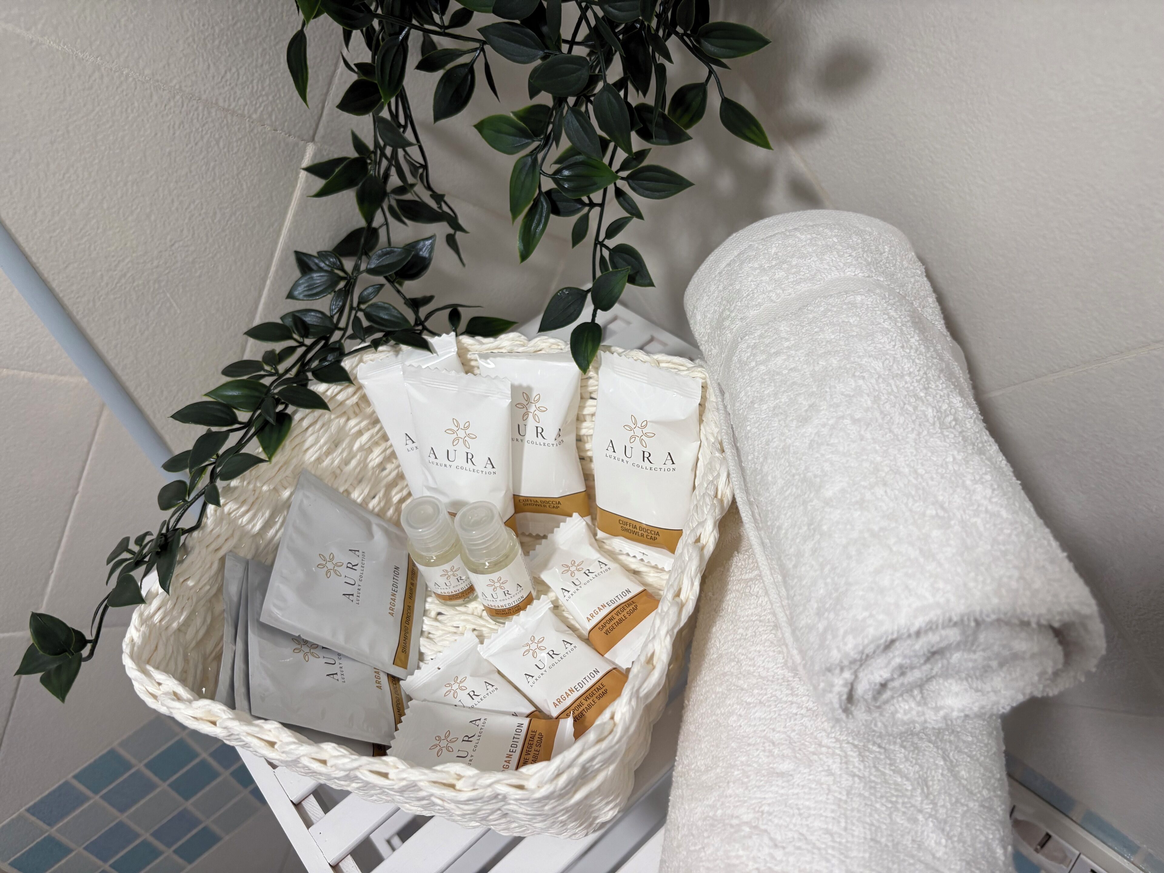 Ein Badezimmer mit weißem Handtuch, einem weißen Korbwäscher mit verschiedenen Pflegeprodukten und einer Pflanze mit grünen Blättern.