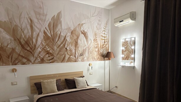 A bedroom with a large bed, a nightstand, a lamp, an air conditioner, and a window with curtains.