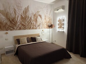A bedroom with a large bed, a nightstand, a lamp, an air conditioner, and a window with curtains. - LuXia Apartment – Your Elegant and Comfortable Stay in Messina (Messina)