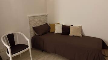 Ein kleines, ordentlich eingerichtetes Schlafzimmer mit einem Einzelbett, einem weißen Stuhl und einem weißen Kopfteil.