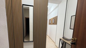A hallway with a wooden panel wall, a mirror, a small table with a vase, and a door with a keypad lock.