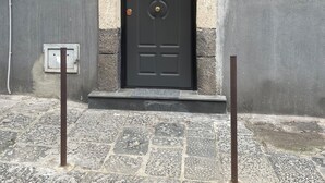 A black door with a number 62 sign above it, a small window with metal bars, and a stone-paved entrance with two metal poles. - 1940 Apartment (Catania)