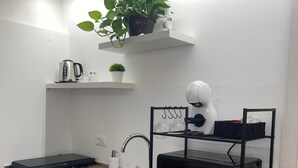 A compact kitchen with a sink, a microwave, a kettle, and a small refrigerator. There is a shelf with a plant and a kettle on it. - 1940 Apartment (Catania)