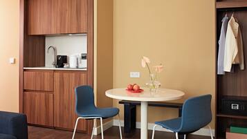 A compact living space with a kitchenette, two blue chairs, a small round table, and a vase with flowers.
