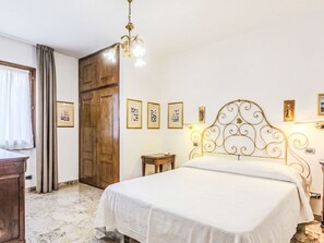 A bedroom with a bed, a wooden wardrobe, a chandelier, and framed pictures on the wall.