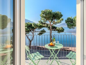 A balcony with a table set for two, a bottle of wine, and a glass. There are two green chairs and a bench. - Lovely apartment for 6 guests with WIFI, TV, balcony and pets allowed (Domaso)
