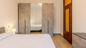 A bedroom with a large bed, a wardrobe with a mirror, a bedside table with a lamp, and a wooden door with a yellow patterned panel.