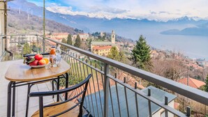 A balcony with a table and chairs, overlooking a mountainous landscape and a lake.