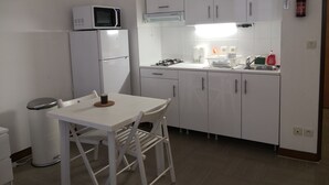 Une cuisine compacte avec des meubles blancs, un four à micro-ondes, un réfrigérateur, un évier et une table à manger avec des chaises.
