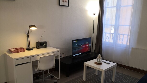 Une petite pièce bien éclairée, avec un bureau, une chaise et un téléviseur qui diffuse une scène nocturne.