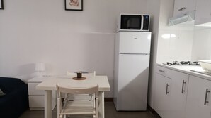 Une cuisine compacte avec un réfrigérateur blanc, un four à micro-ondes et une cuisinière. On y trouve une petite table avec une chaise et une tasse à café.