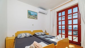 A double bed with a dark bedspread, two matching pillows, a wooden nightstand, and a wall-mounted air conditioner. - Apartman Mistral 3 (Crikvenica)