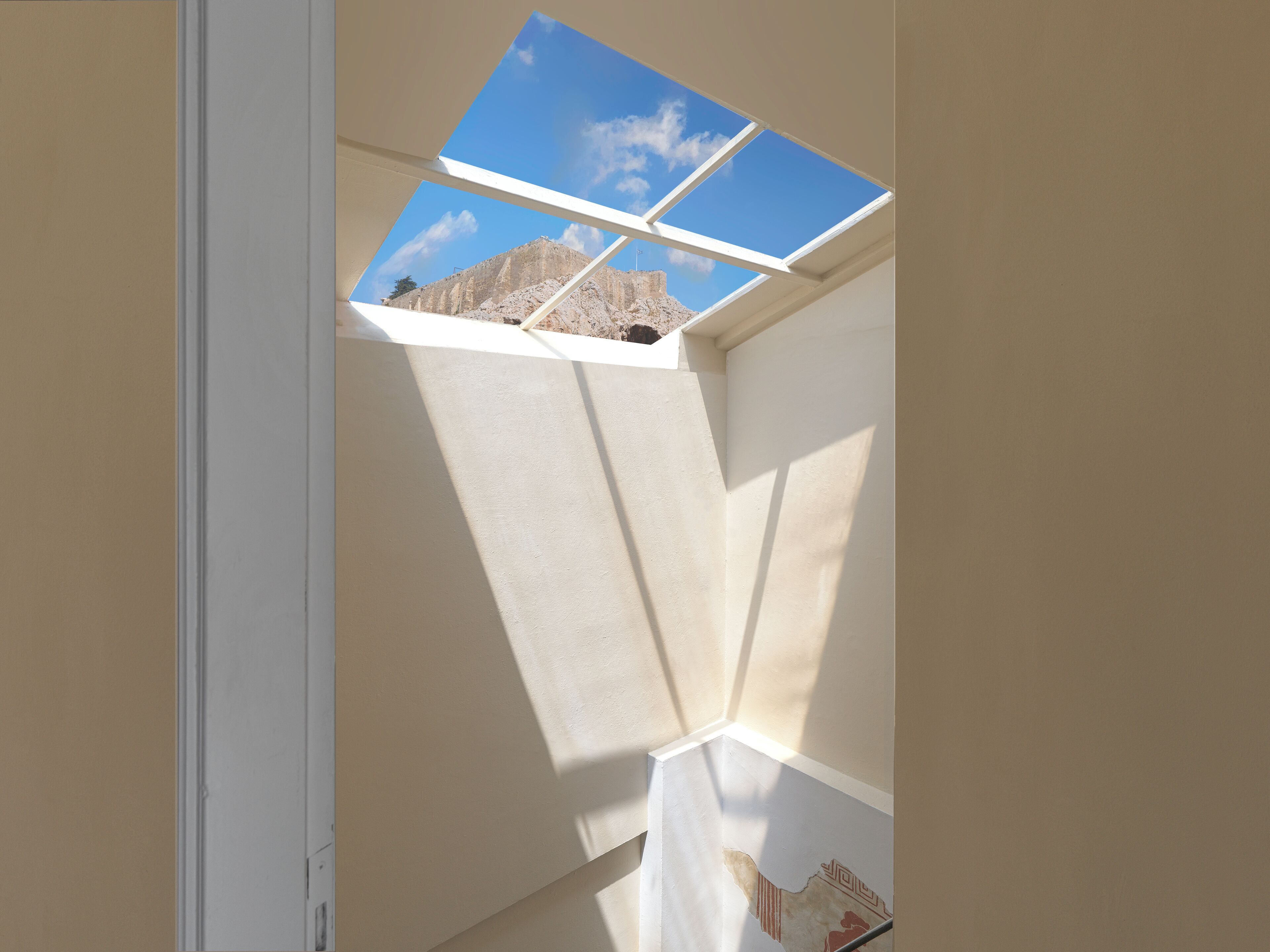A room with a skylight, a white wall, and a partial view of a mountain.