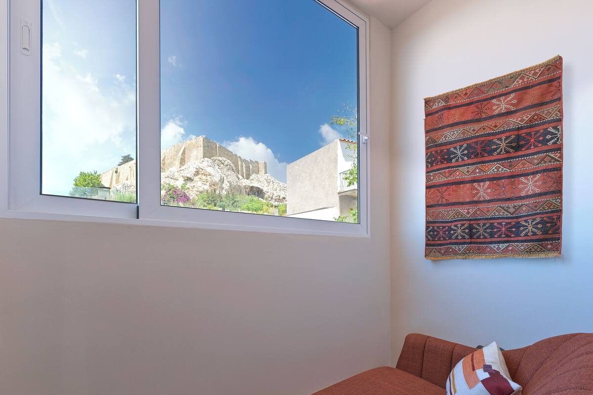 A room with a large window, a bed with a red blanket, and a patterned tapestry on the wall.