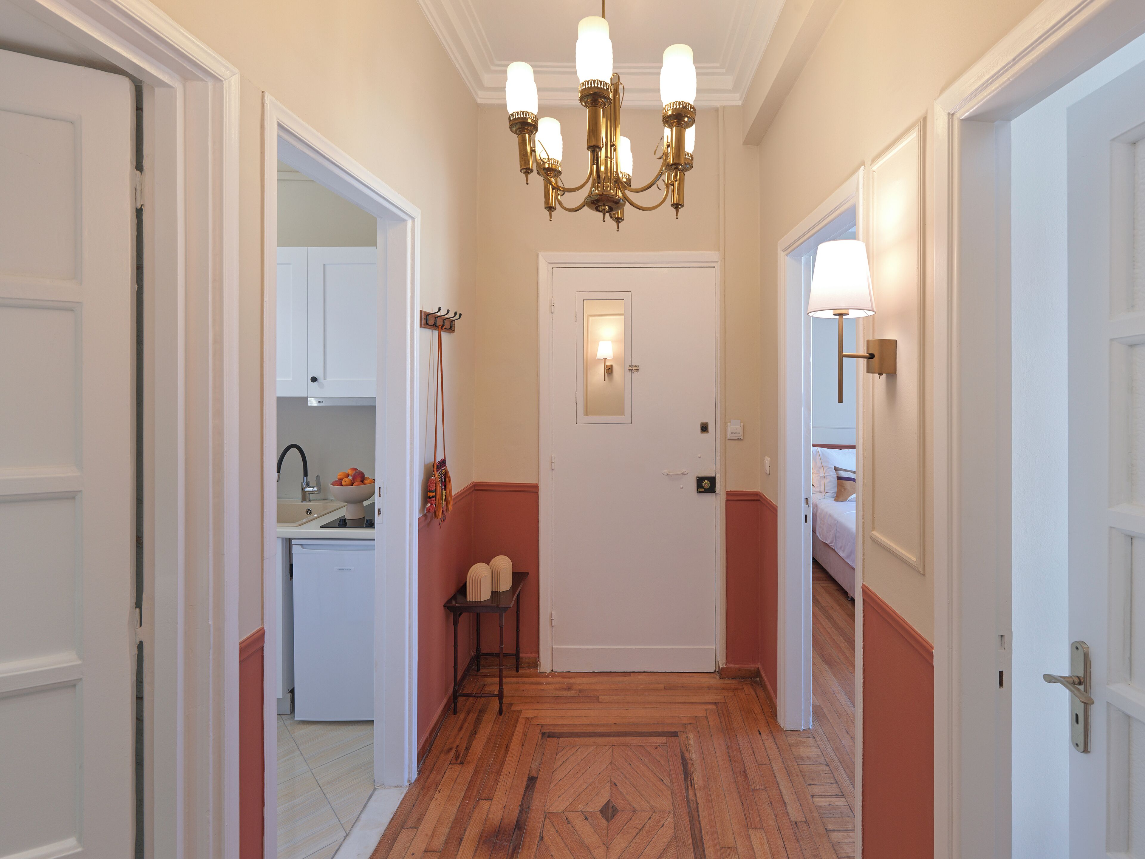 A hallway with a wooden floor, white doors, and a chandelier.