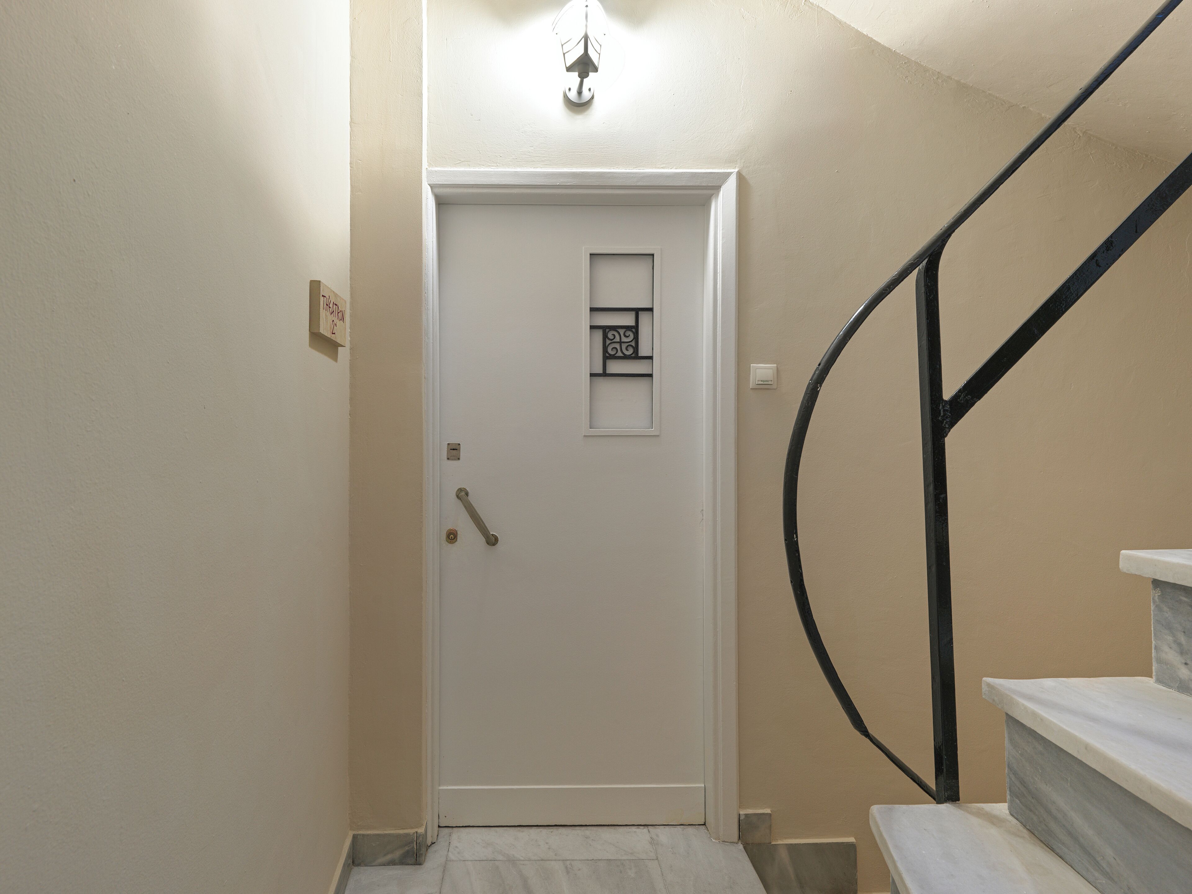 Une porte blanche avec une petite fenêtre, une main courante et un luminaire au-dessus.
