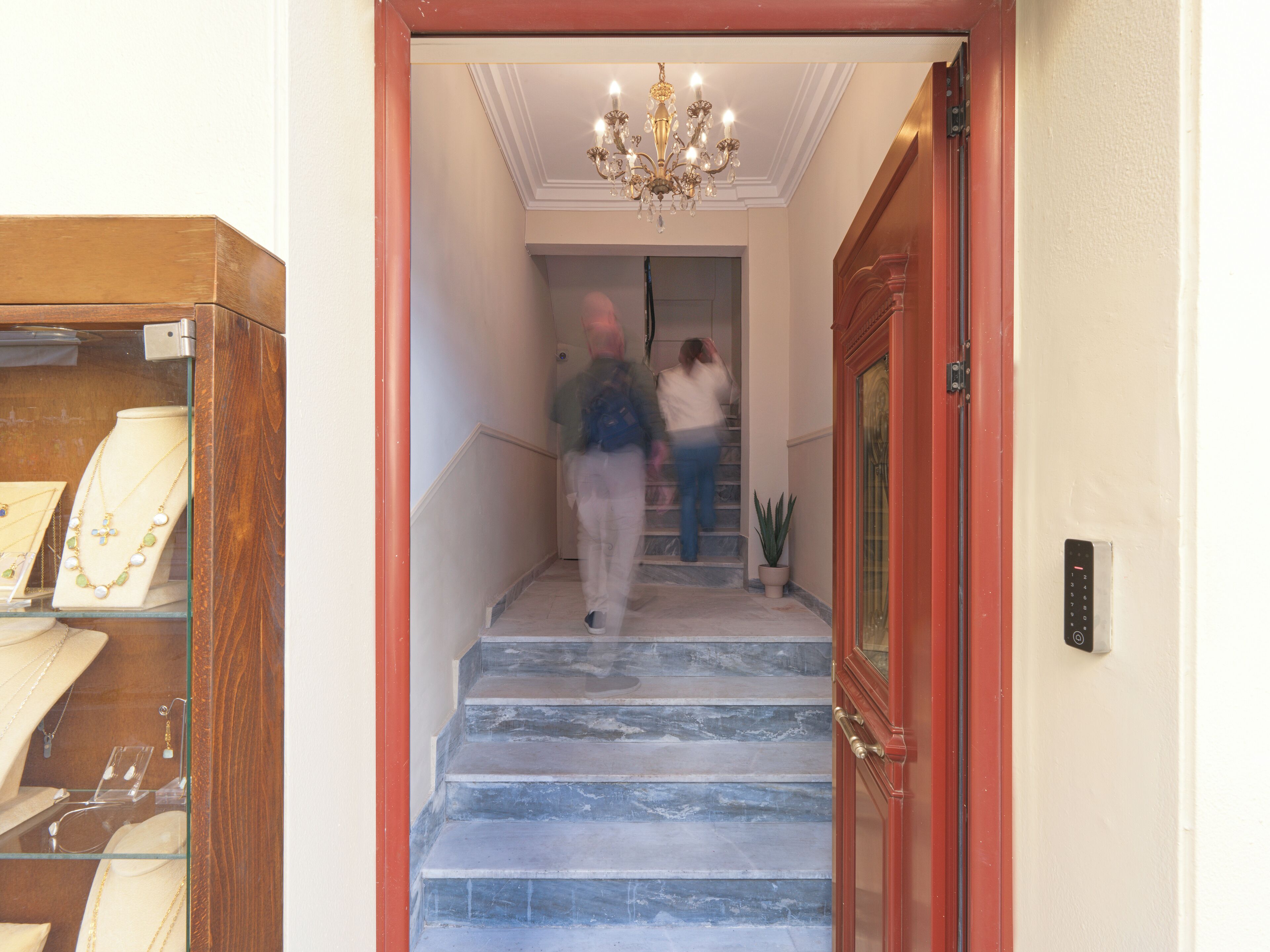 Een marmeren trap die leidt naar een kamer met een kroonluchter, een kamerplant en een sieradenvitrine.