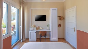 Habitación de hotel con cama, escritorio con computadora, televisor y vistas al balcón exterior.