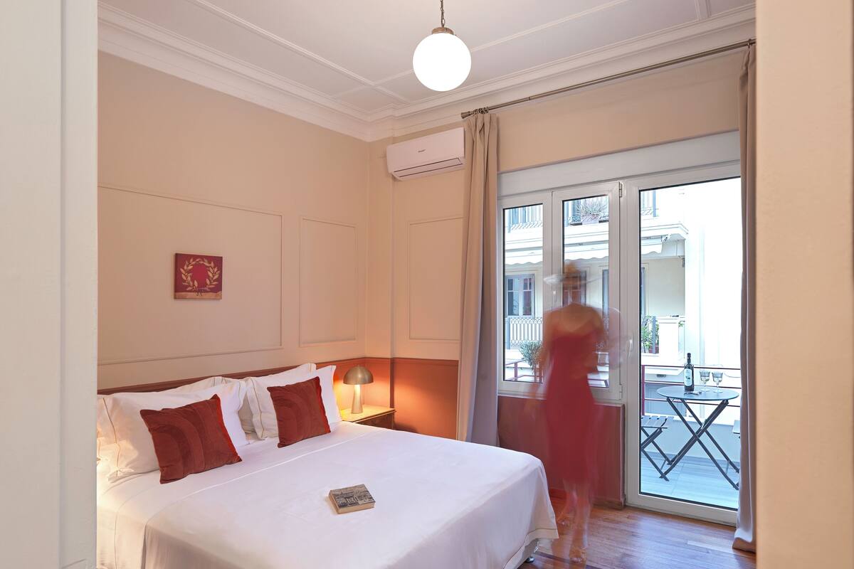 A hotel room with a bed, a nightstand, a lamp, and a view of the outside balcony.