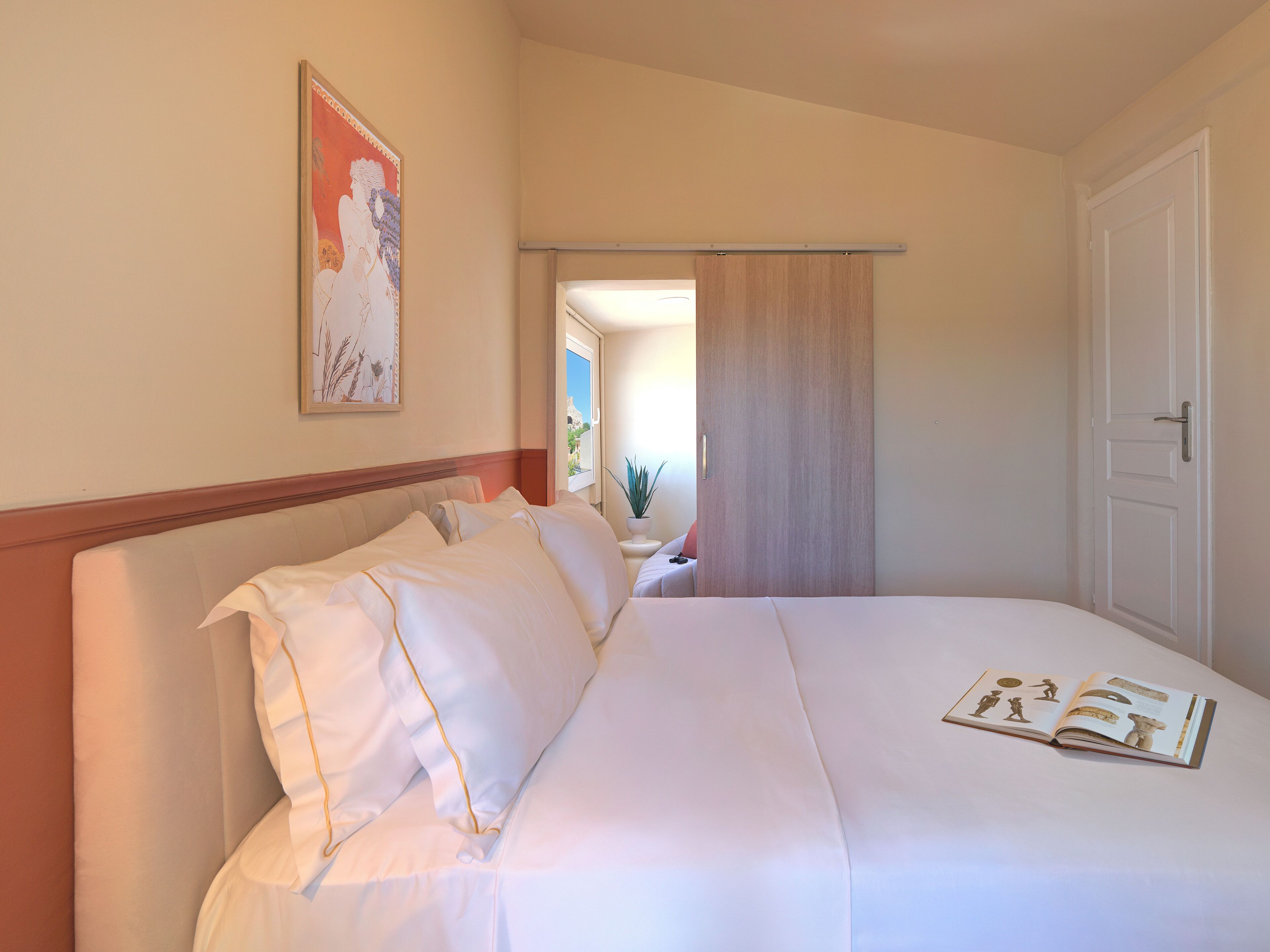A neatly made bed with white linens and pillows, a framed picture on the wall, and a book on the bed.