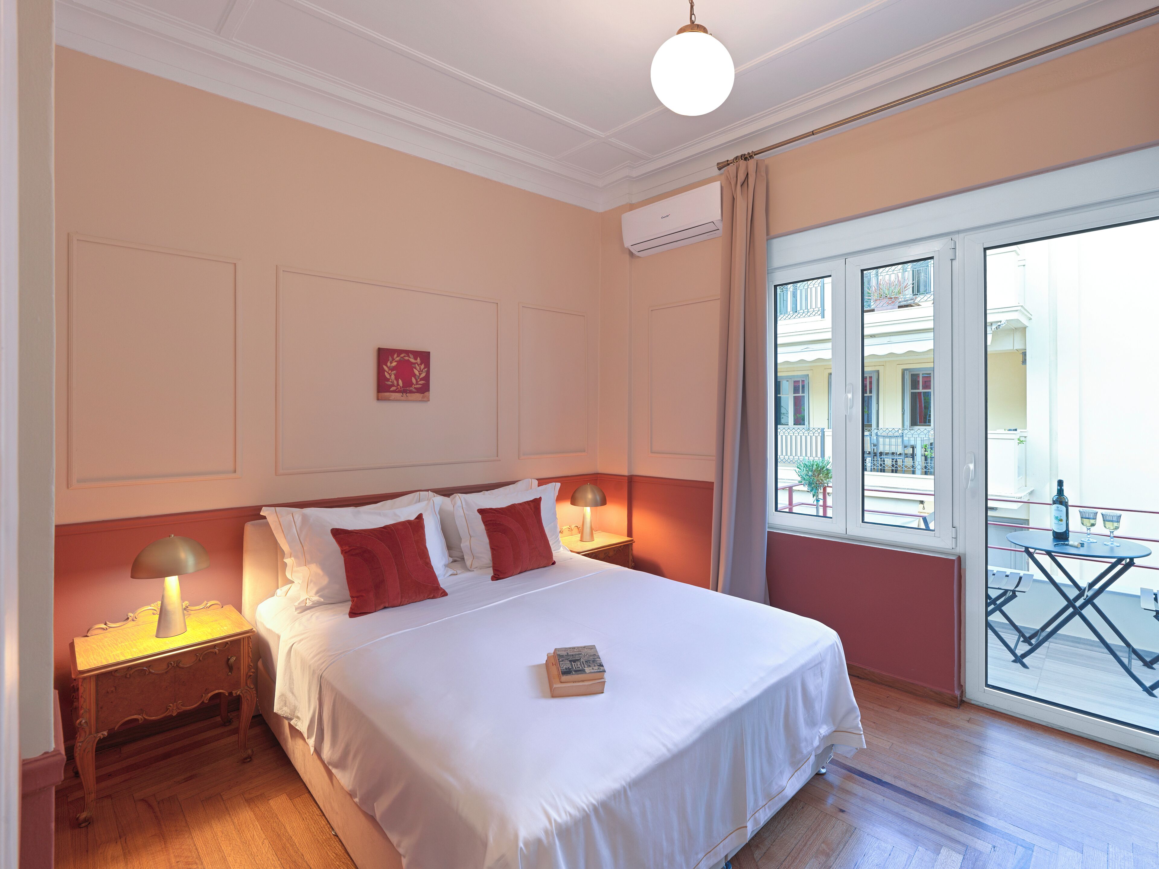 A hotel room with a large bed, two bedside tables with lamps, a window with a view of the outside, and a small balcony.