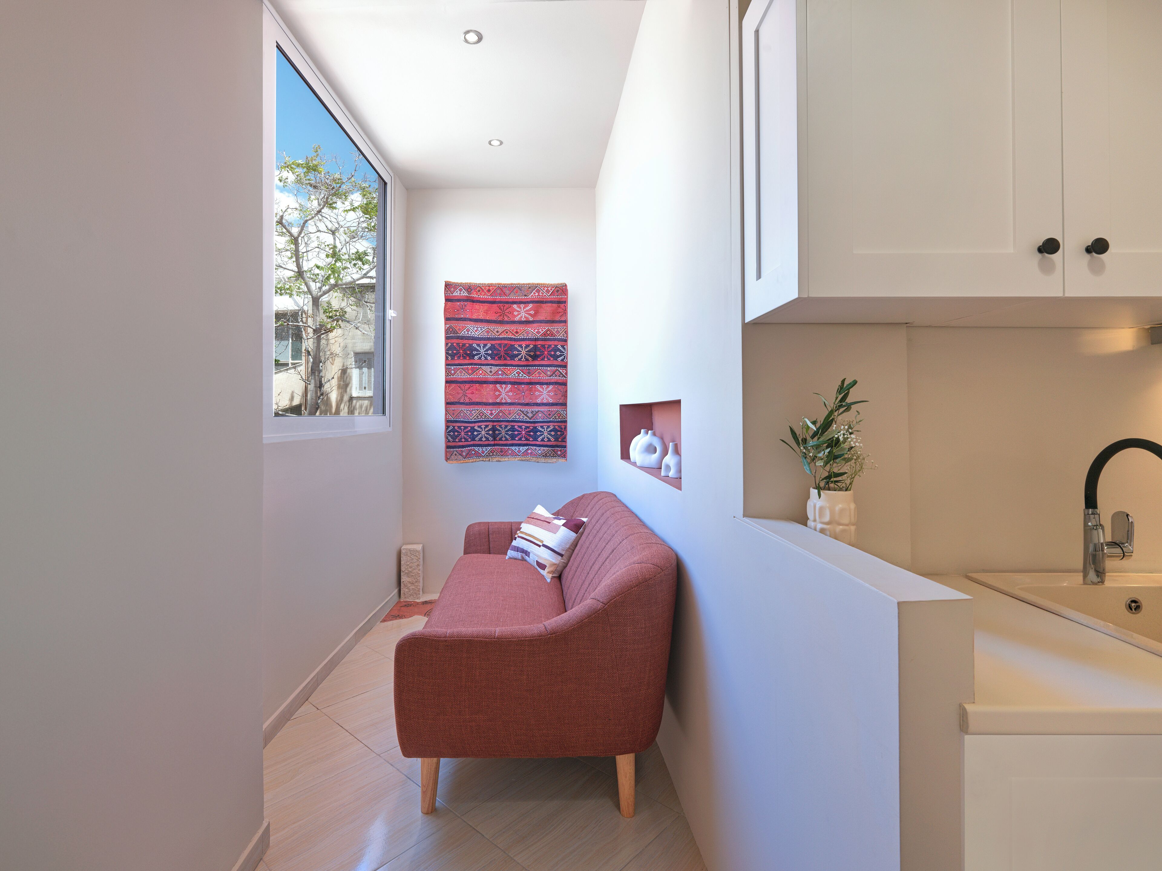 A modern interior with a red sofa, a patterned tapestry, and a minimalist kitchen with a sink.