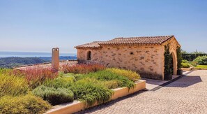 A stone building with a tiled roof, surrounded by a garden with various plants and flowers. - Le Mas d’Azur – Exceptional view & pool (Tourrettes-sur-Loup)