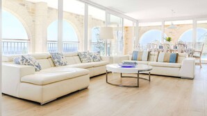 A modern living room with a large sofa set, a coffee table, and large windows offering a view of stone arches. - Le Mas d’Azur – Exceptional view & pool (Tourrettes-sur-Loup)