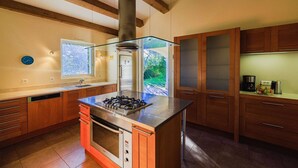 Une cuisine moderne avec des meubles en bois, un îlot central doté d’une cuisinière à gaz et une vue sur la verdure environnante.