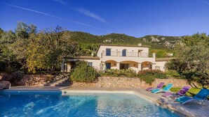 Une piscine avec des chaises longues, un mur en pierre et un bâtiment doté d’un balcon.