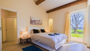 Une chambre à coucher avec un lit, une table de chevet, une lampe et une vue sur l’extérieur.