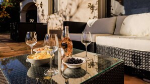Une table avec des verres à vin, une bouteille et des bols remplis de collations, le tout installé à l’extérieur, avec un canapé en osier et un bâtiment en arrière-plan.