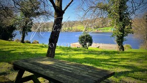 Une table de pique-nique en bois, située dans un espace verdoyant, agrémenté d’arbres et offrant une vue sur un lac.