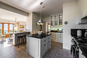 A kitchen with a central island, bar stools, a stove, and a view of the outdoors.