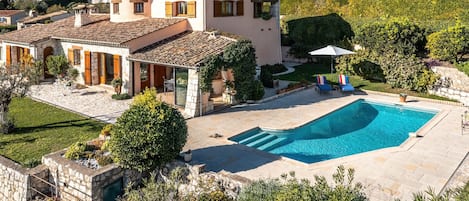 A villa with a swimming pool, stone architecture, and a well-maintained garden.