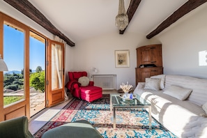 A spacious living room with a red armchair, white sofa, and a glass coffee table.