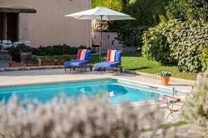 A swimming pool with two lounge chairs and an umbrella.