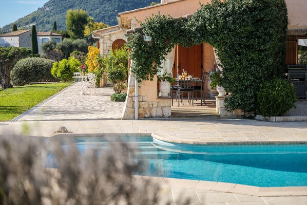 A poolside area with a stone pool, outdoor seating, and a view of a hillside.