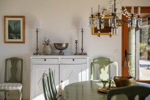 A dining area with a white cabinet, two green chairs, a table with a bowl and candle, and a chandelier. - Villa Virettes – Peaceful haven with pool (Tourrettes-sur-Loup)